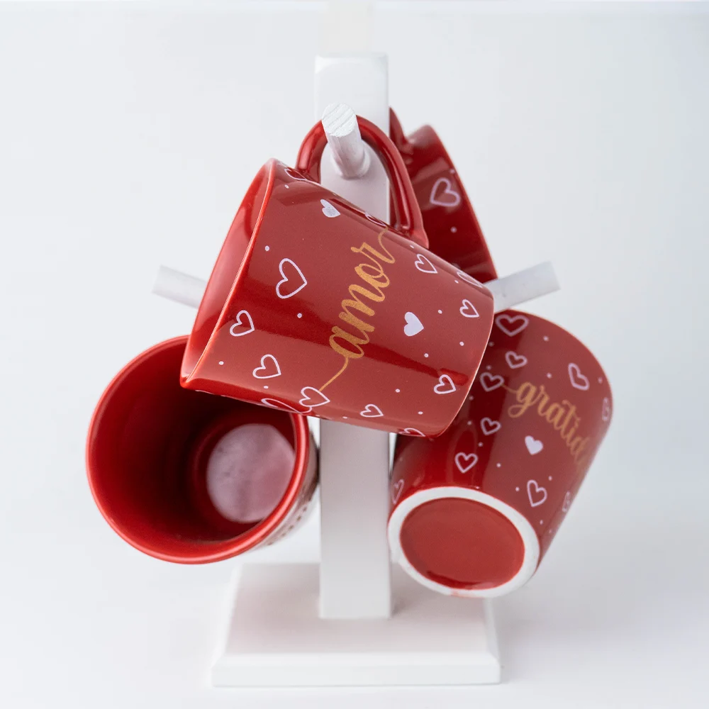 Caneca vermelha com a palavra amor em dourado pendurada em suporte branco com outras canecas.