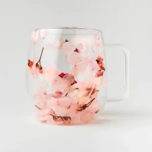 Caneca de vidro borossilicato transparente com flores secas rosa suave e coral preservadas, vista frontal com alça sobre fundo branco